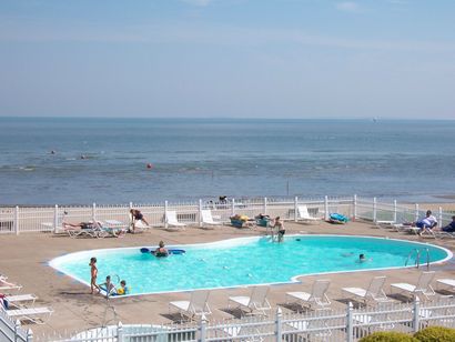 A large swimming pool surrounded by chairs and a fence with a view of the ocean