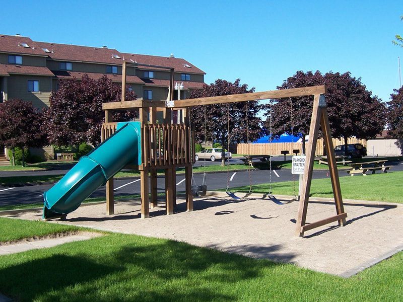 A playground with a slide and swings in front of a building