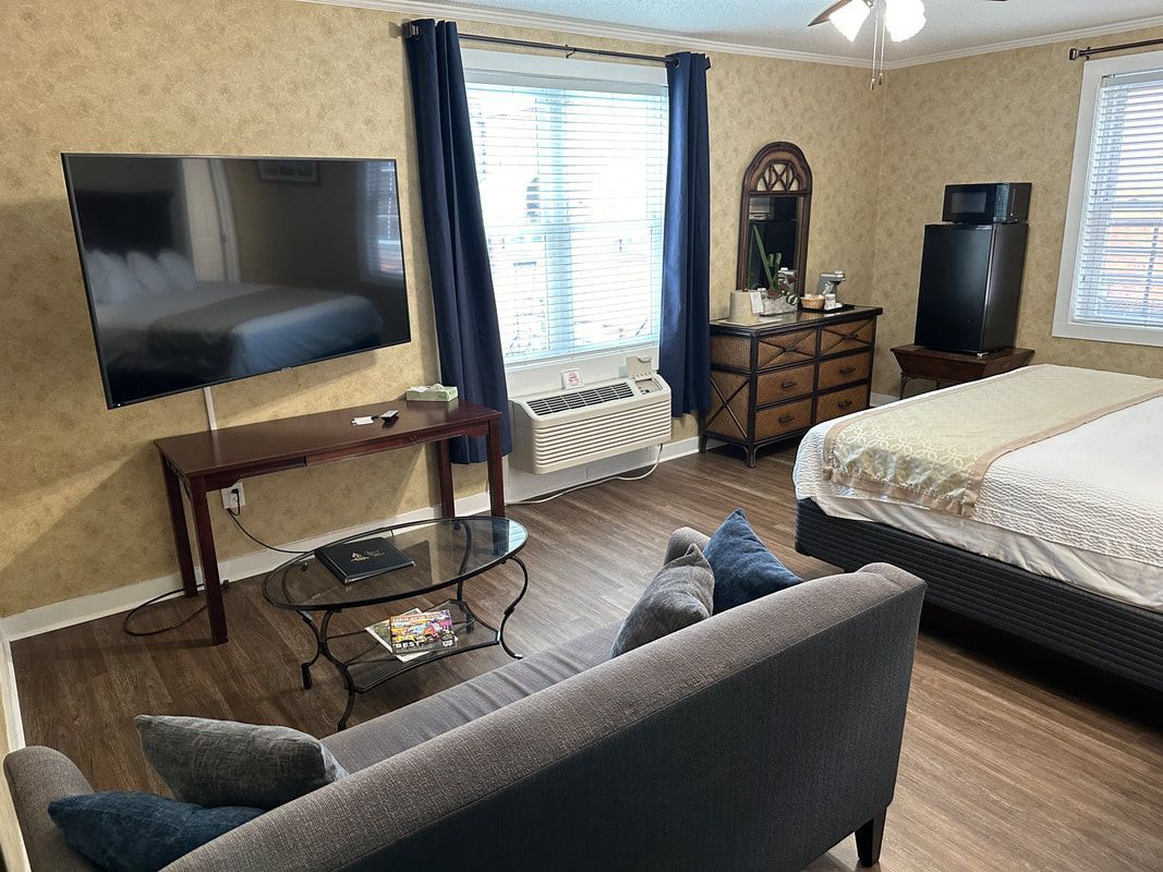 A hotel room with a couch , television , dresser and bed.