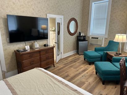 A hotel room with a bed , chairs , ottomans and a flat screen tv.