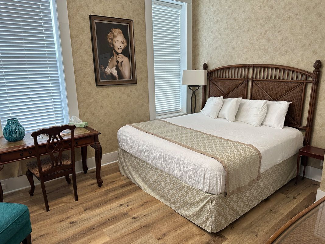 A bedroom with a bed , desk , chair and a painting on the wall.