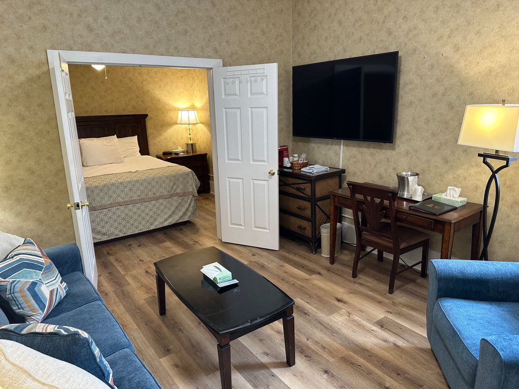 A hotel room with a couch , chair , desk and television.