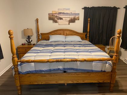 A bedroom with a bed , nightstand , lamp and paintings on the wall.