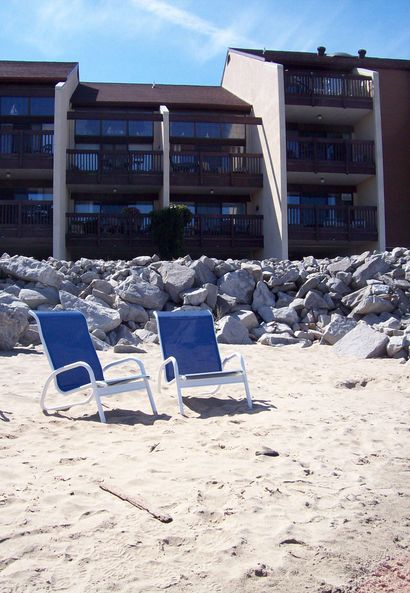 Two blue chairs are on the beach in front of a building