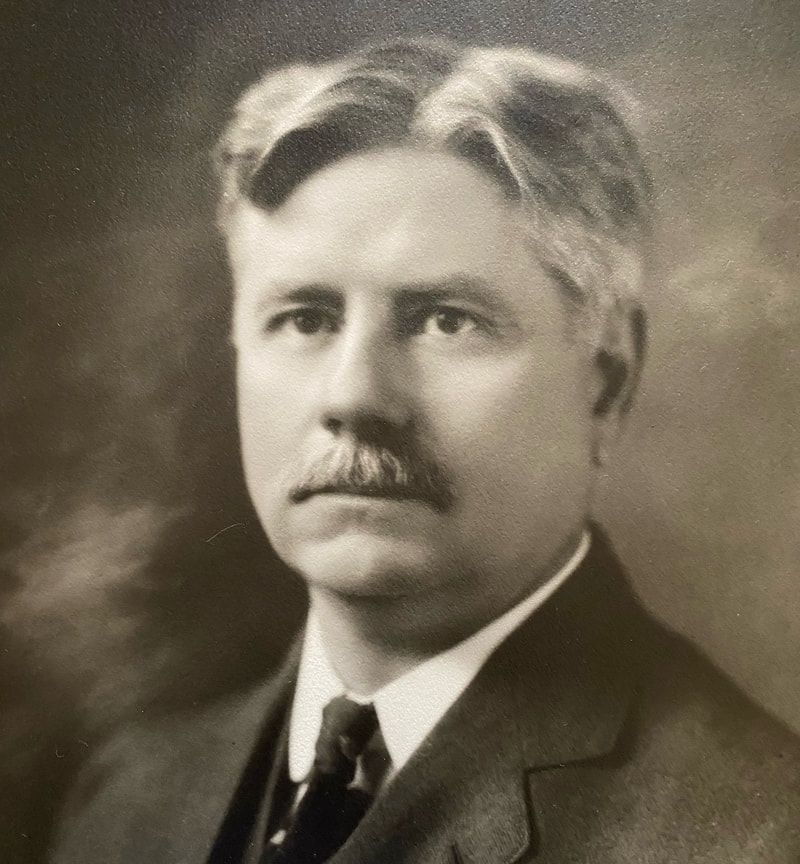 A man with a mustache is wearing a suit and tie.