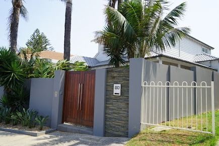 A House With A Fence And A Wooden Gate Surrounded By Palm Trees — Rendering By Yilmaz P/L In Wollongong, NSW