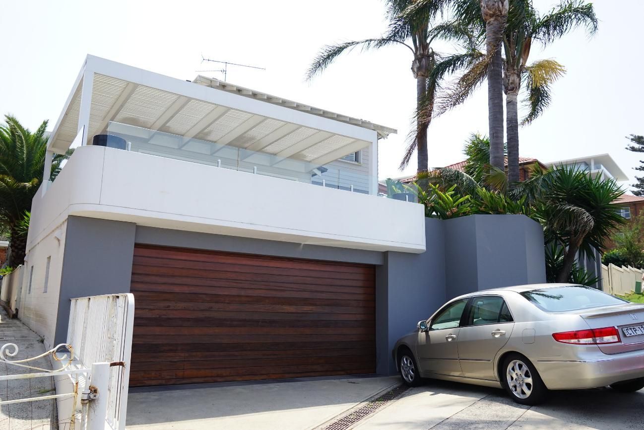 A Car Is Parked In Front Of A House With A Wooden Garage Door — Rendering By Yilmaz P/L In Albion Park, NSW