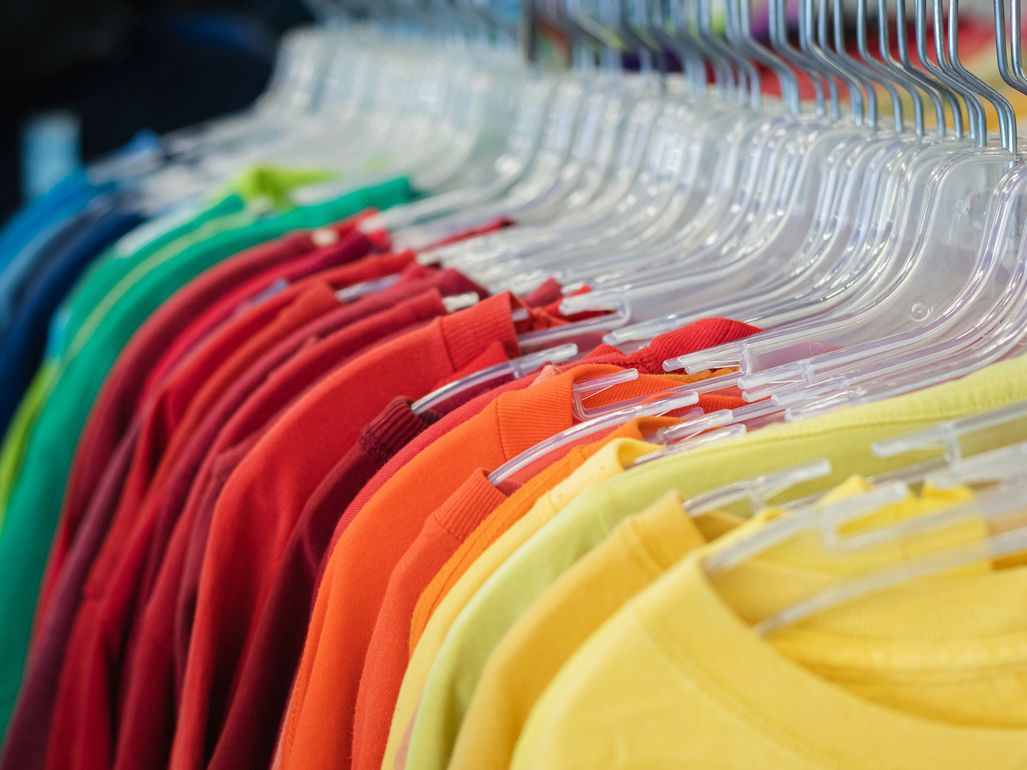 Una fila de camisas coloridas colgadas de perchas de plástico transparente en una tienda.