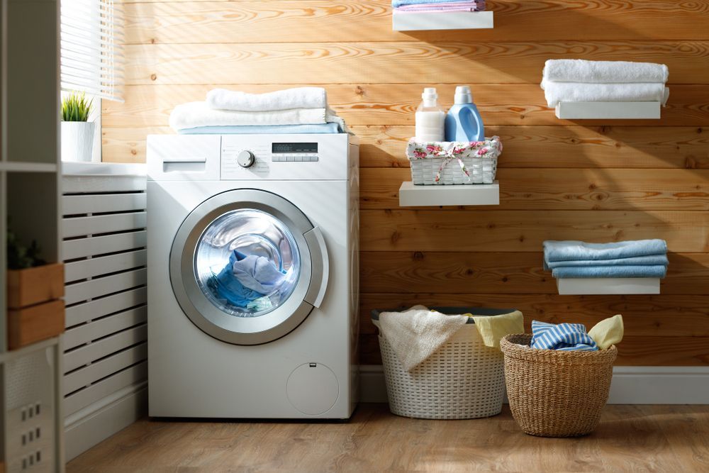 A Washing Machine is Sitting in a Laundry Room Next to a Basket of Clothes — Suncoast Kitchens In Kunda Park, QLD