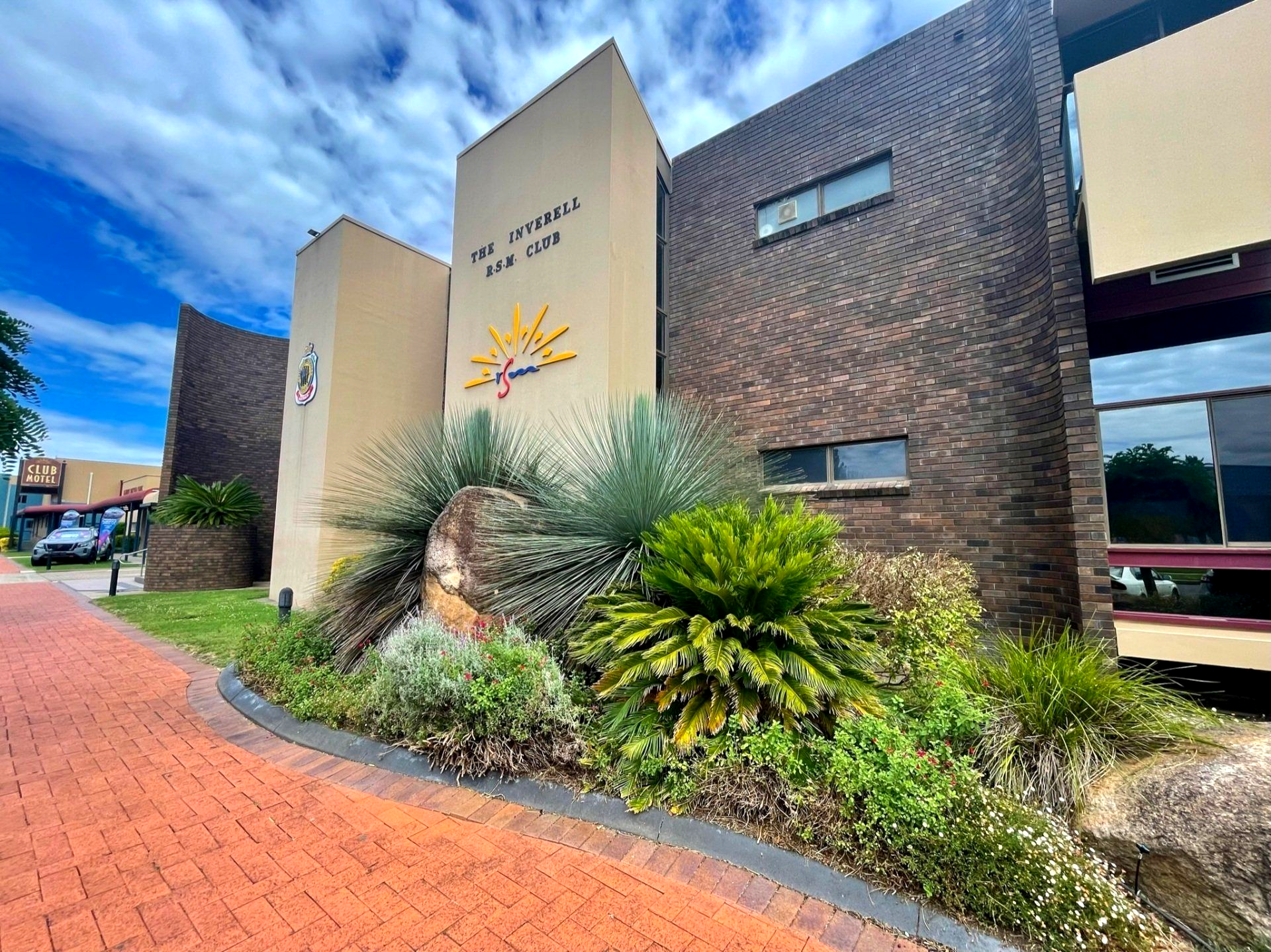 Building exterior with signage "The Tyrell Inn" and a sun symbol, featuring brickwork, greenery, and blue sky.