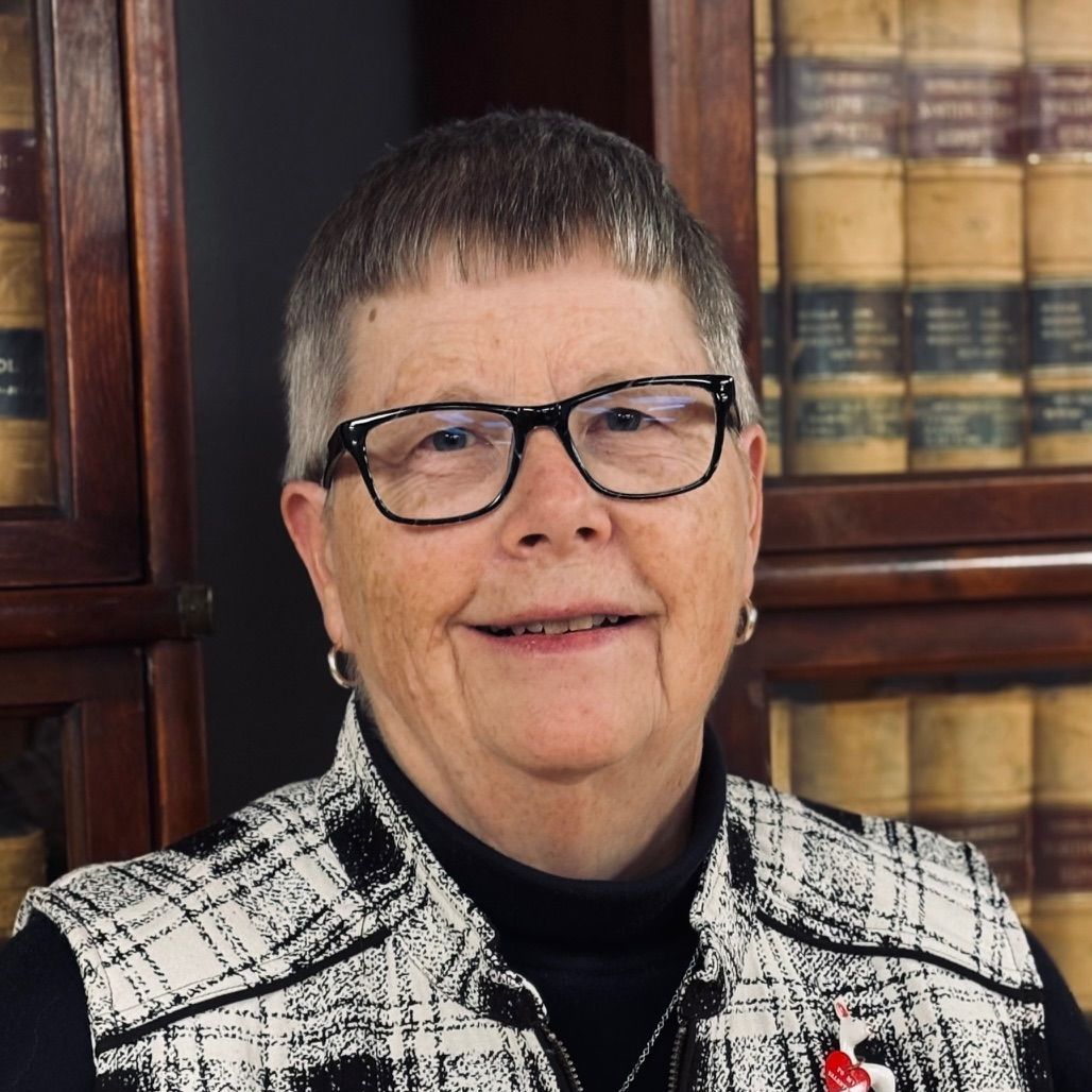 A woman wearing glasses and a scarf is standing in front of a wall.