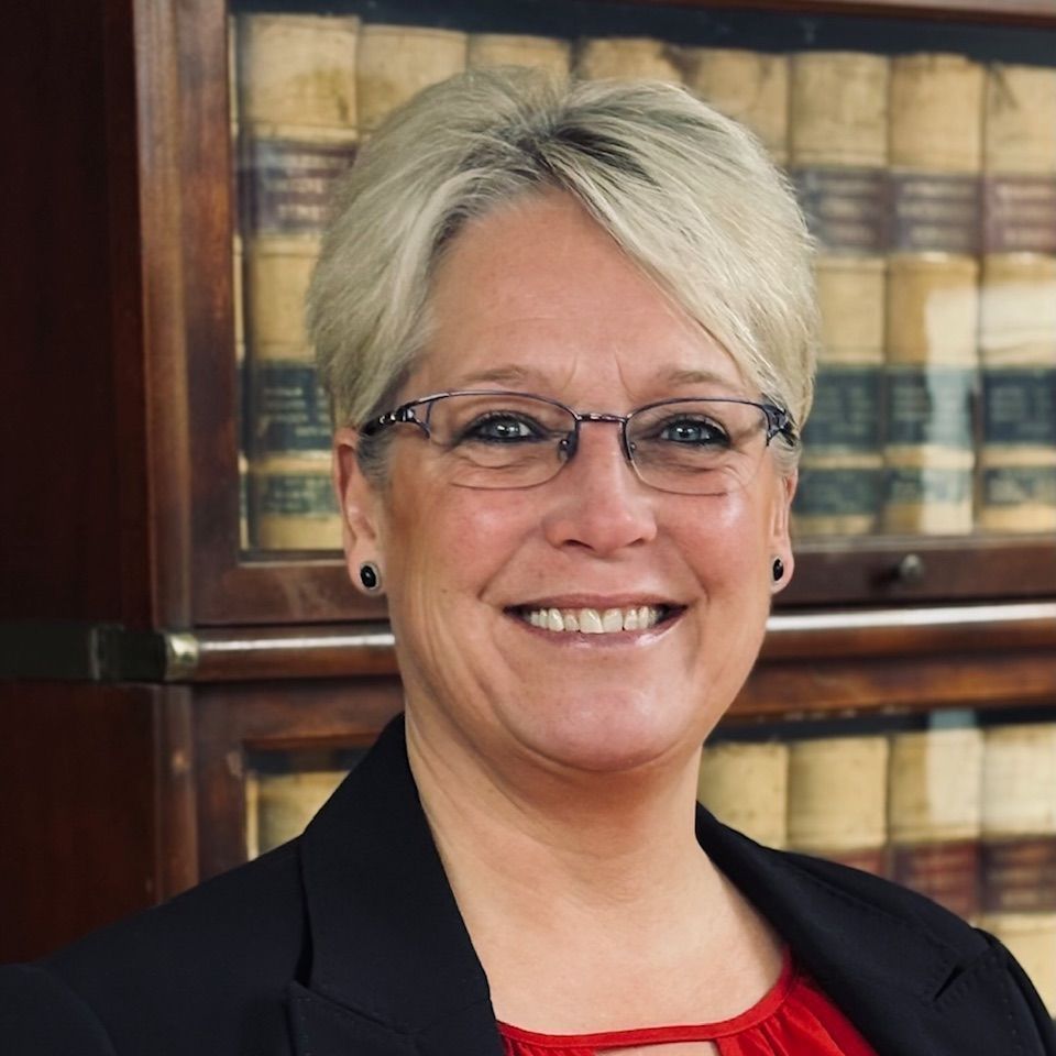 A woman wearing glasses and a blue shirt is smiling for the camera.