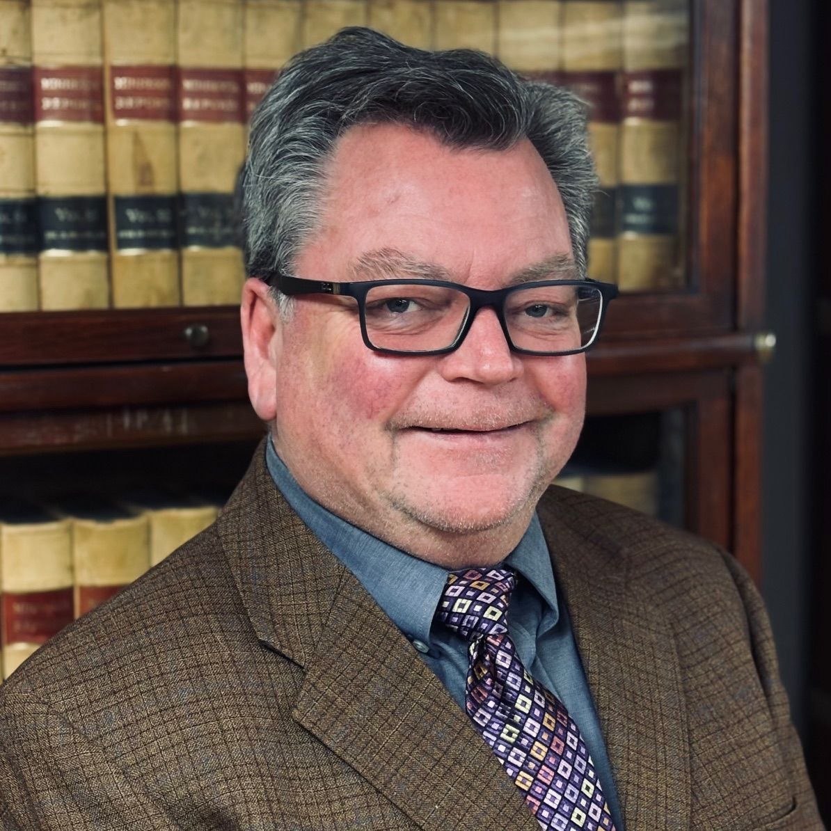 A man wearing glasses and a suit and tie is smiling.