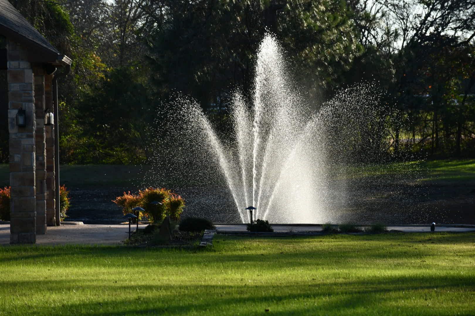 There is a fountain in the middle of a lush green field.