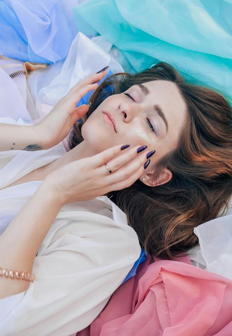 A woman is laying on a pile of clothes with her eyes closed.