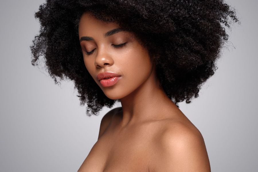 A woman with a large afro is looking down with her eyes closed.