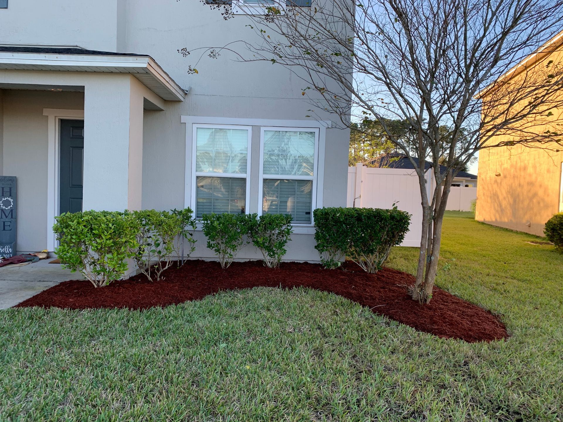 A house with green bushes and a tree in front, mulched beds, and a grassy lawn.