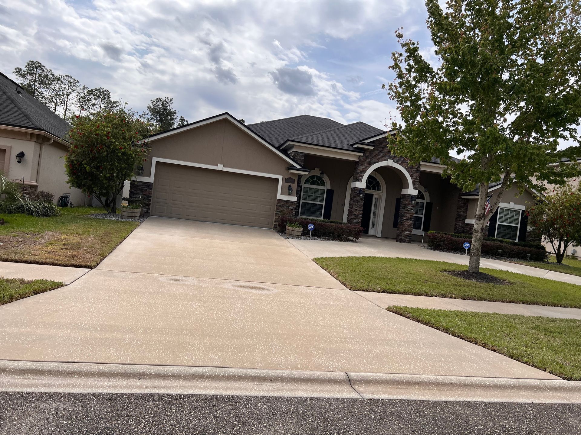 Tan house with a brown roof and garage. Wide concrete driveway and green lawn.