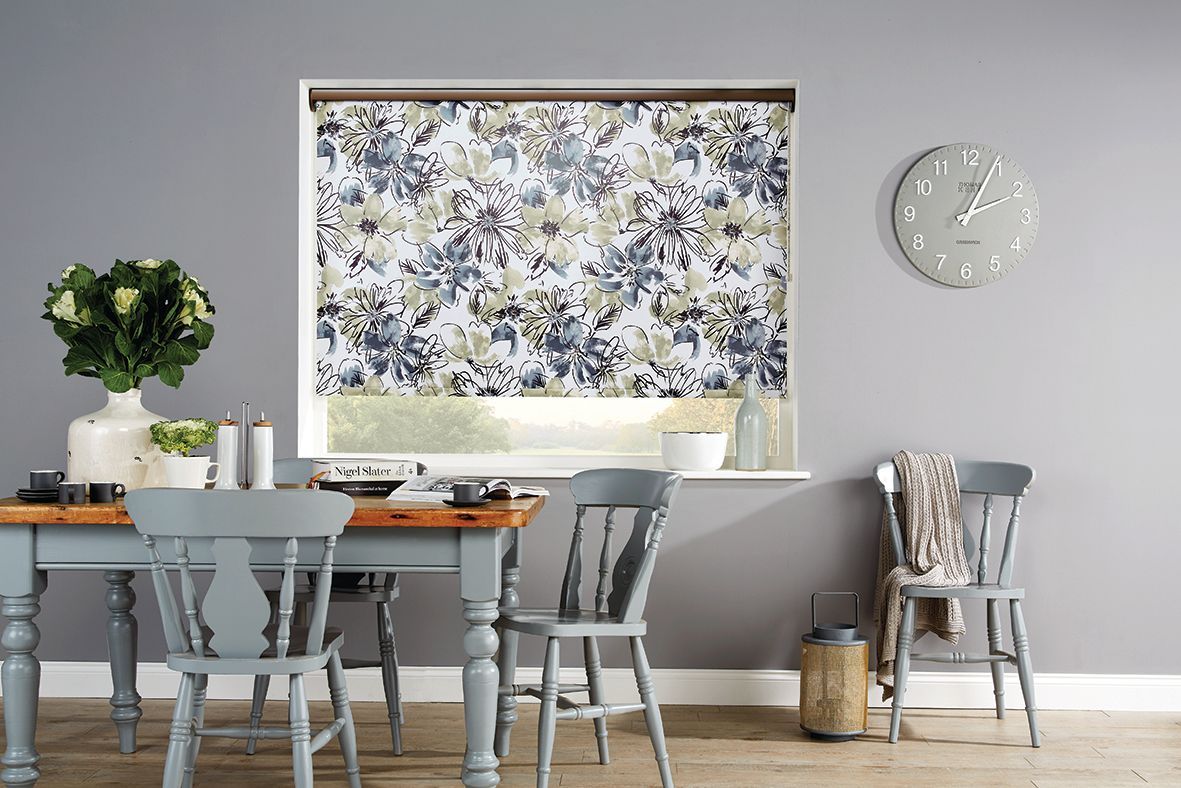 Dining room with table, chairs, floral blind, clock, vase of flowers, and a grey wall. Abundance Blinds In Charmhaven, NSW