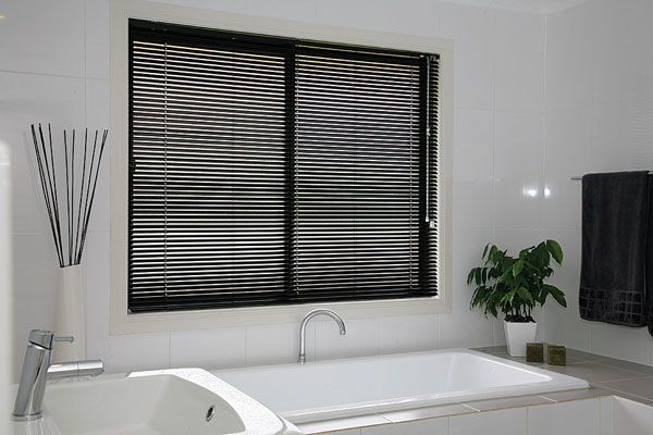 Bathroom With a White Bathtub, Dark Blinds, and a Small Potted Plant Near the Window — Abundance Blinds In Charmhaven, NSW
