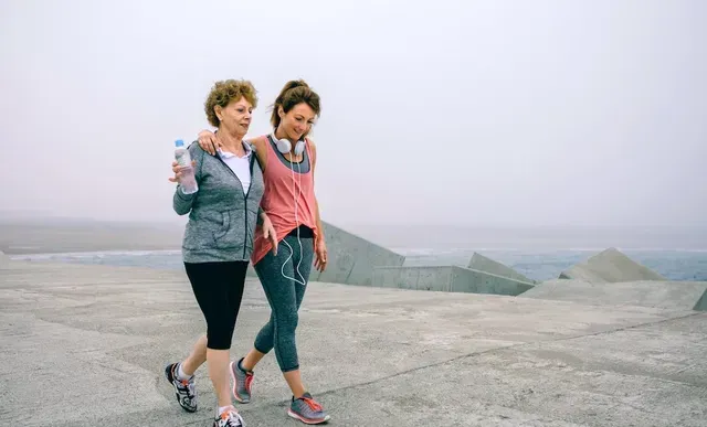 Two women are walking on a pier next to the ocean.