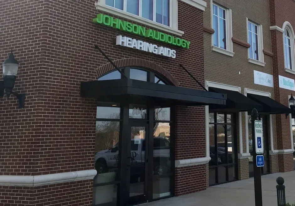 Exterior of Johnson Audiology office with green sign on a brick building; black awnings over windows.