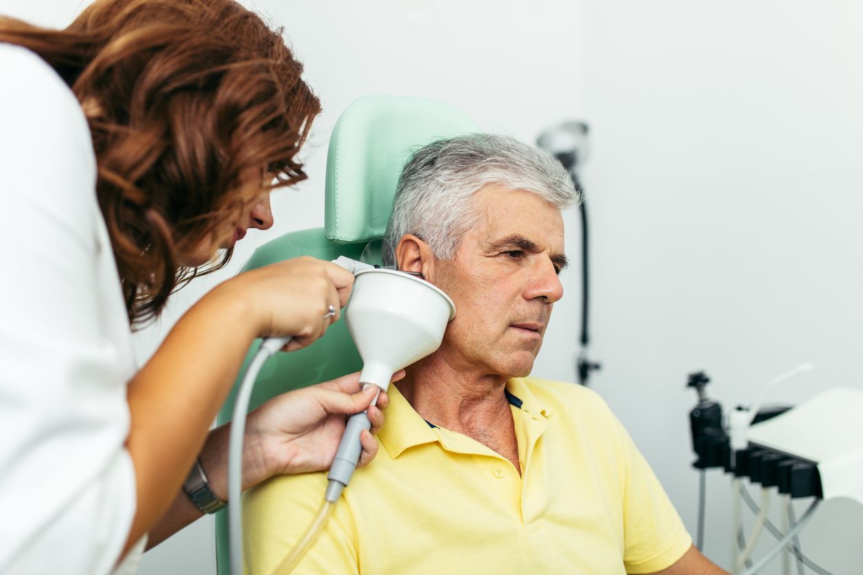 An elderly man is getting an ear exam by an otolaryngologist.