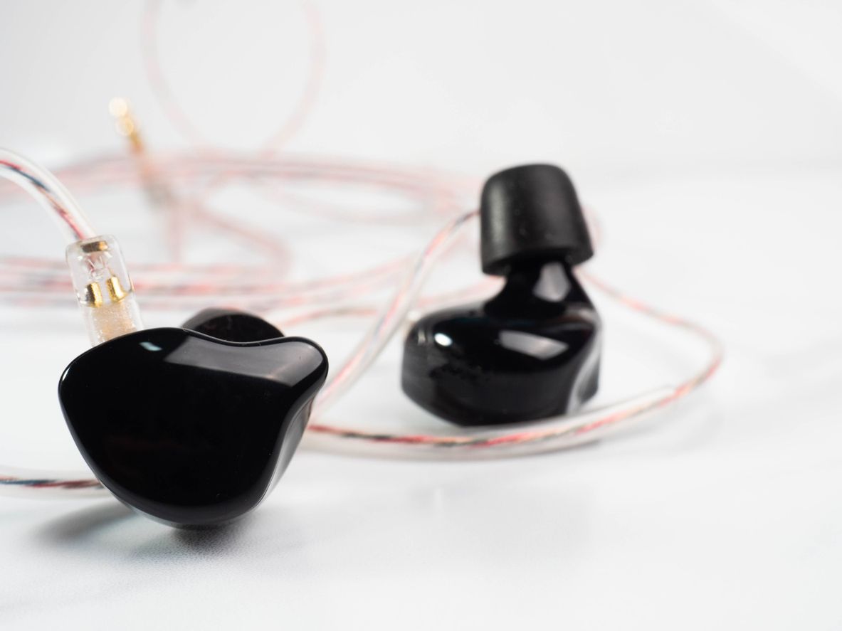 A pair of black in ear headphones are sitting on a white surface.