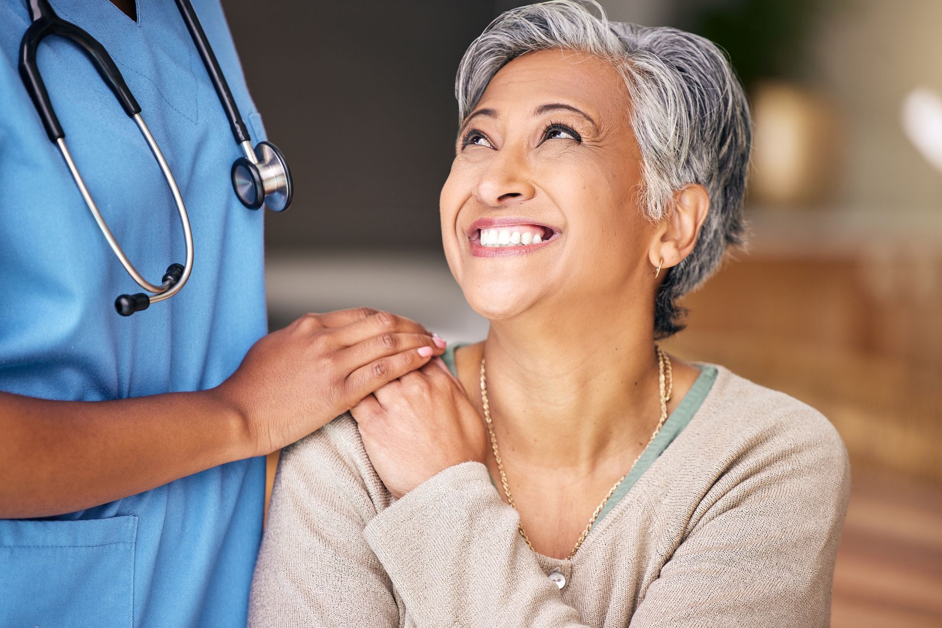 A nurse is holding the hand of an older woman who is smiling.