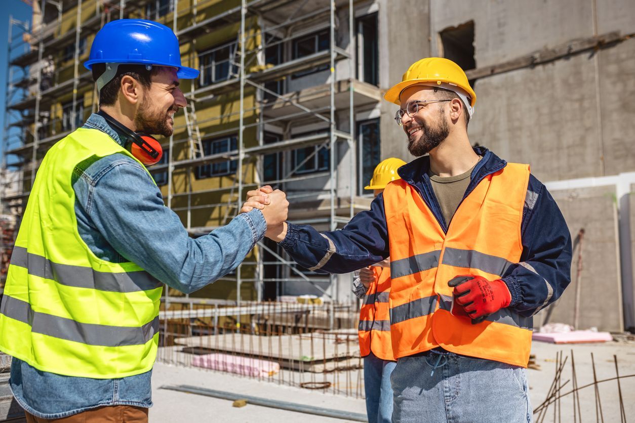 Two construction workers are shaking hands on a construction site.