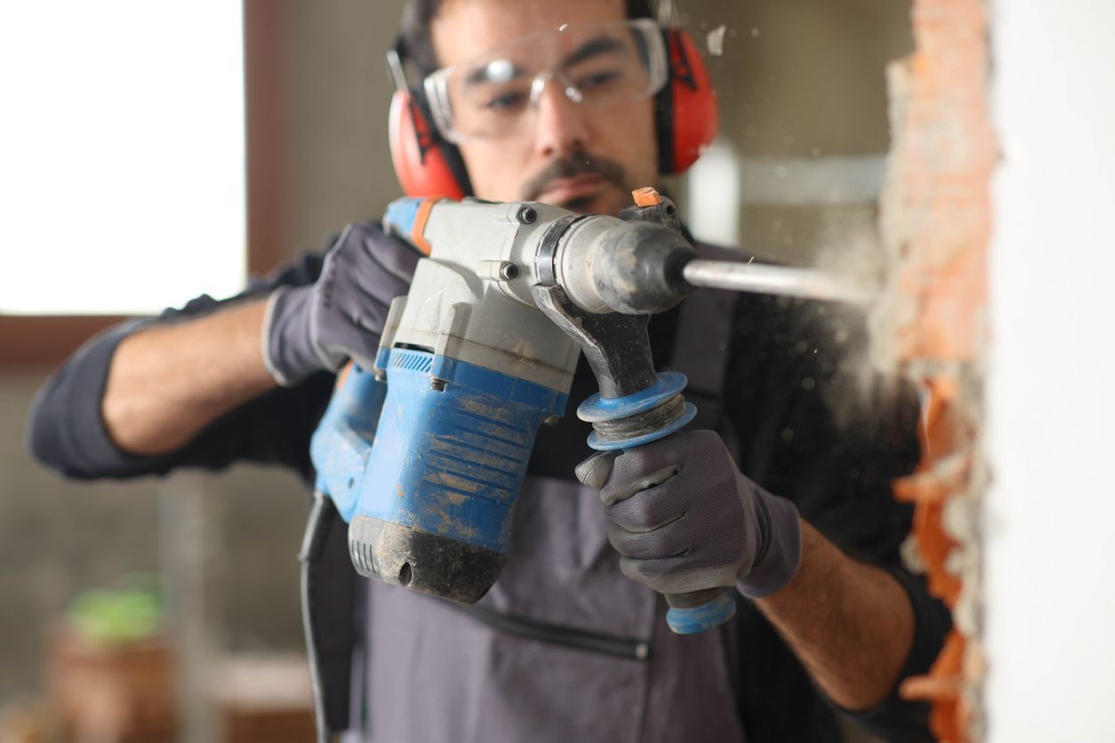 A man is using a hammer drill to drill a hole in a wall.