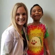 A woman in a lab coat is standing next to a young boy in a taco shirt.