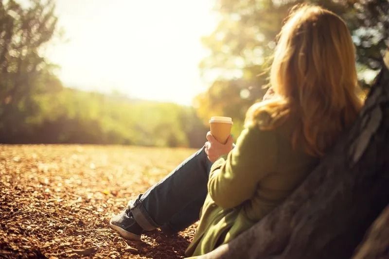 A woman is sitting on a tree trunk holding a cup of coffee.