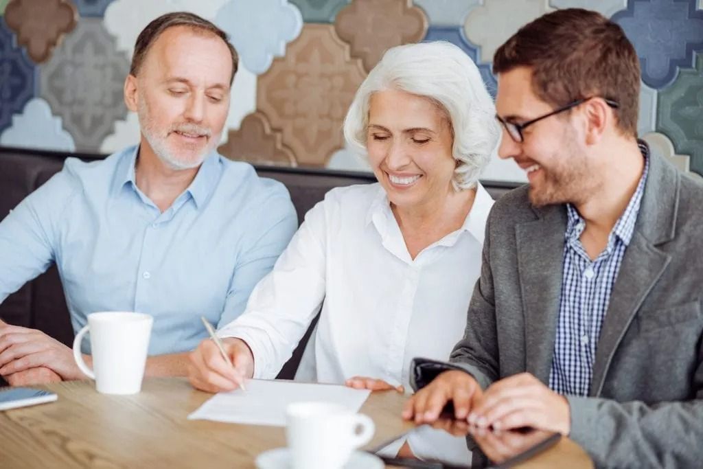 A group of people are sitting at a table looking at a tablet.