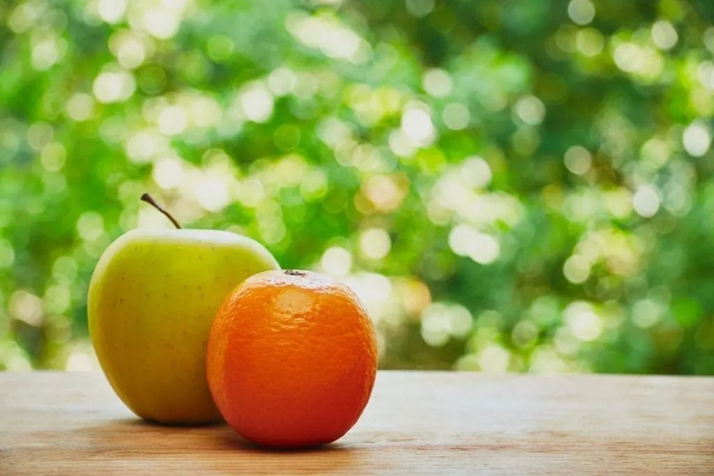 An apple and an orange are sitting on a wooden table.