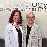 Two women are standing next to each other in front of a sign.