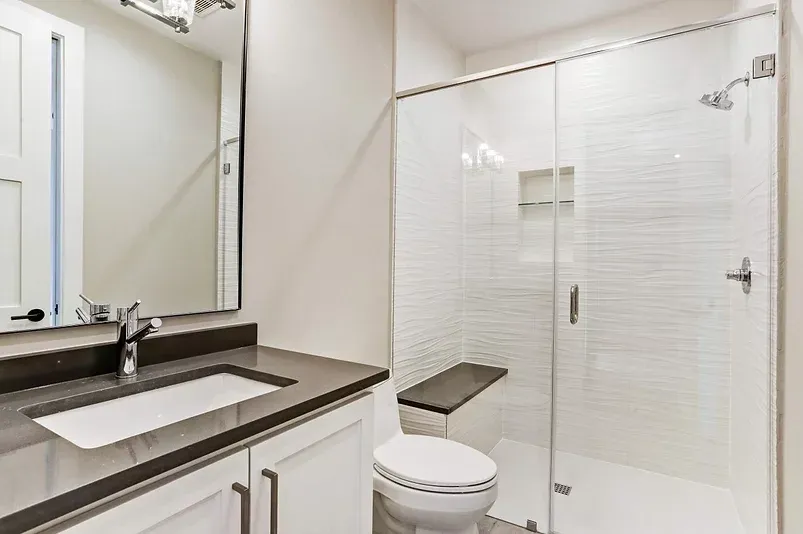 A bathroom with a toilet , sink , mirror and walk in shower.