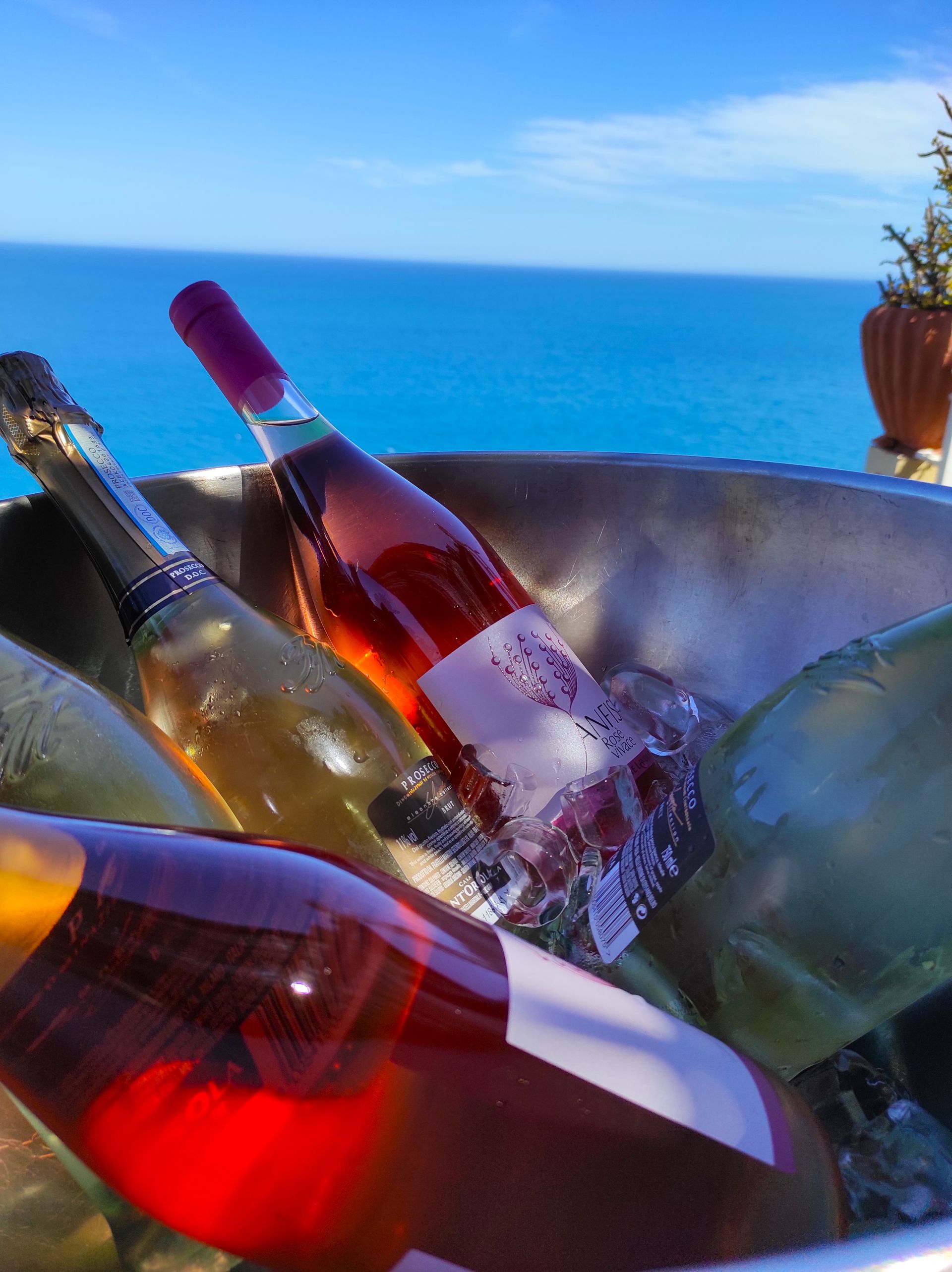 Tre bottiglie di vino in un secchio di ghiaccio con l'oceano sullo sfondo.