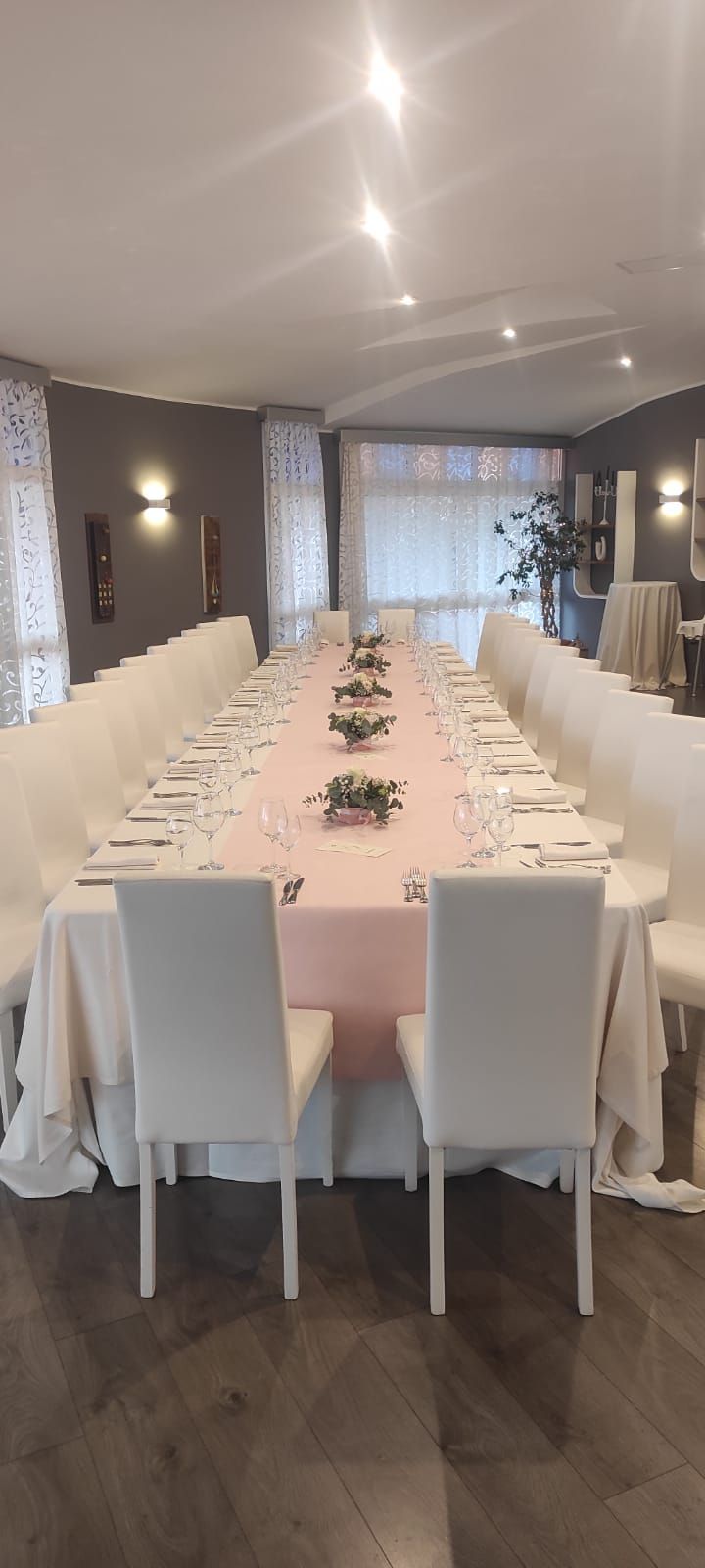 Un lungo tavolo con una tovaglia rosa e sedie bianche in una stanza.