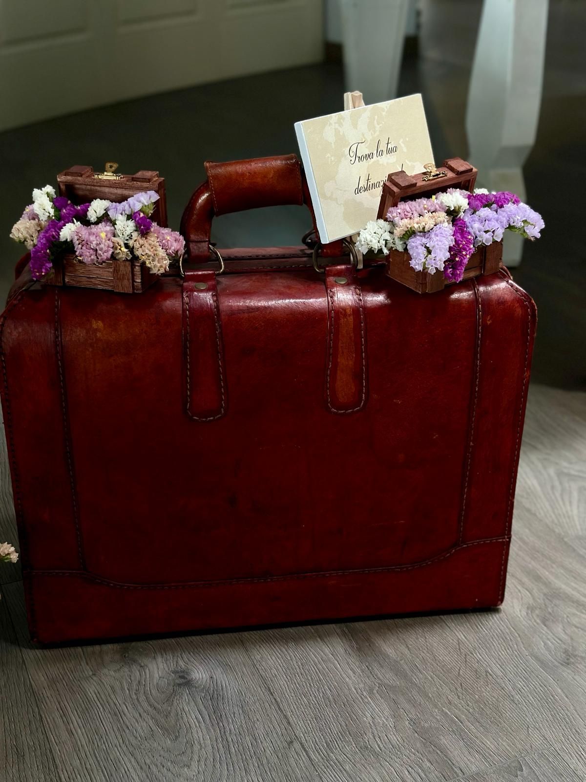 Una valigia rossa con dei fiori sopra è appoggiata su un pavimento di legno.