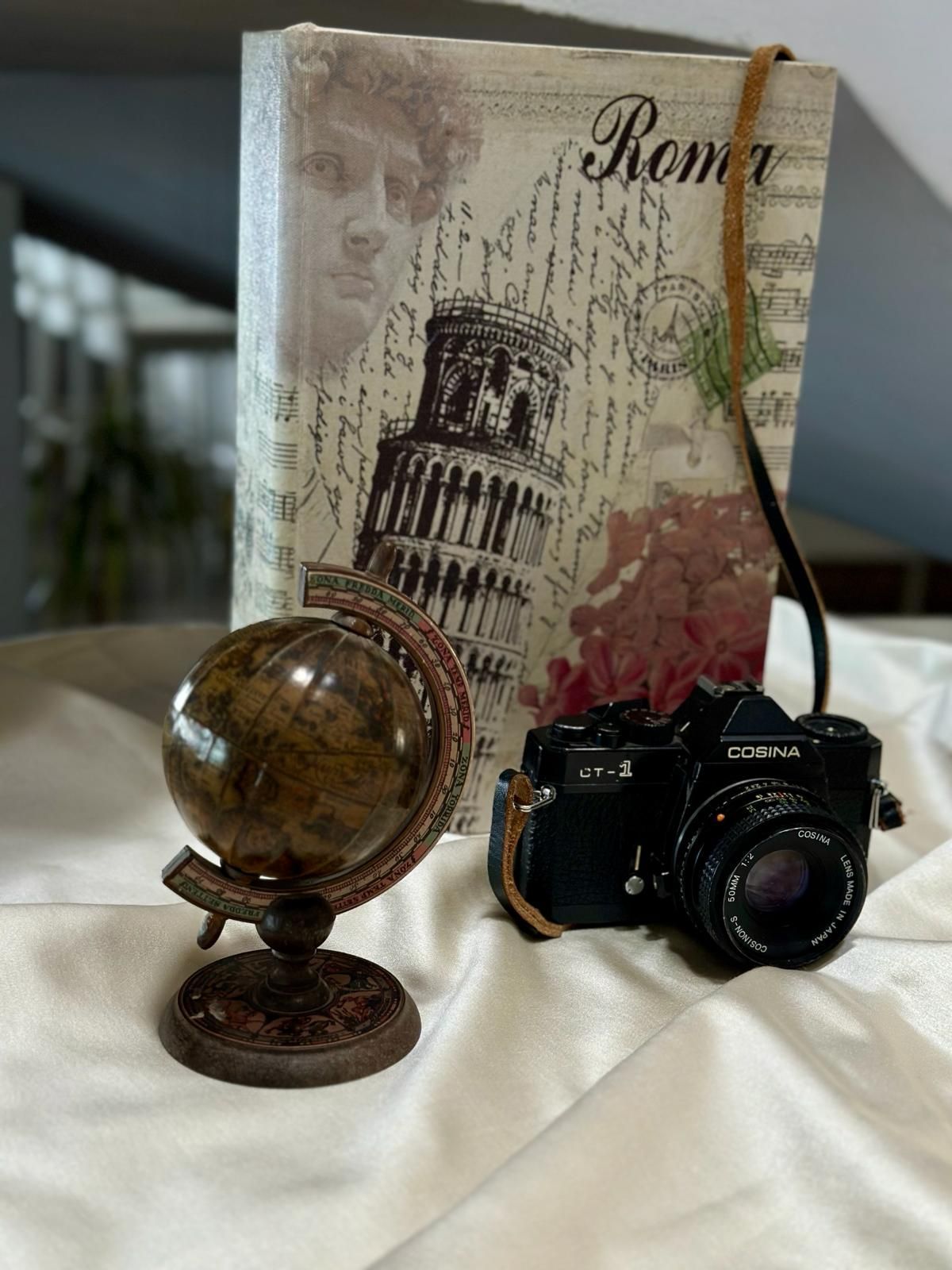 Una macchina fotografica e un mappamondo sono sul letto accanto a un libro.