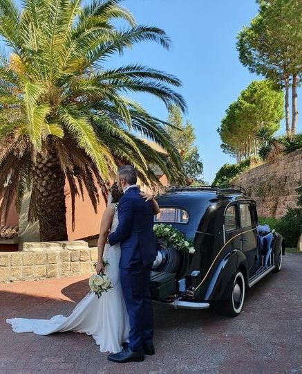 Una sposa e uno sposo si baciano davanti a una vecchia macchina.