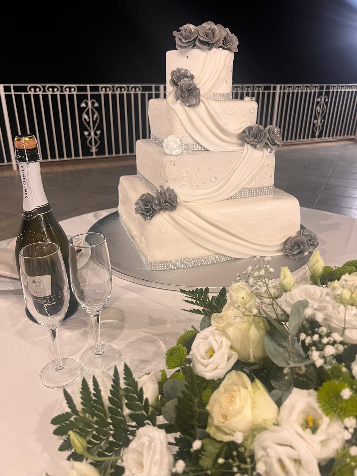 Una torta nuziale è appoggiata su un tavolo con dei fiori e una bottiglia di champagne.