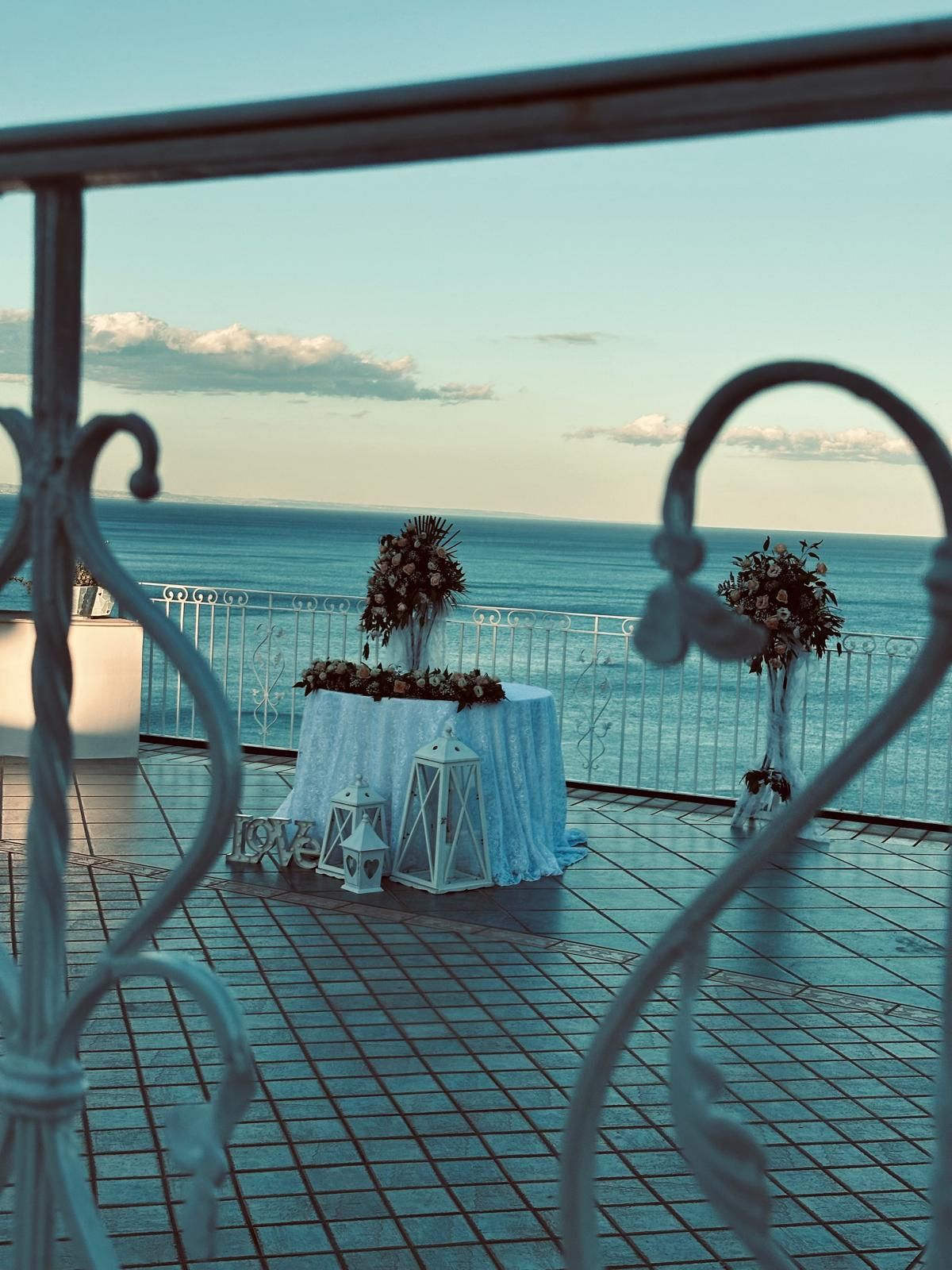 Un tavolo con dei fiori sopra è appoggiato su un balcone che si affaccia sull'oceano.