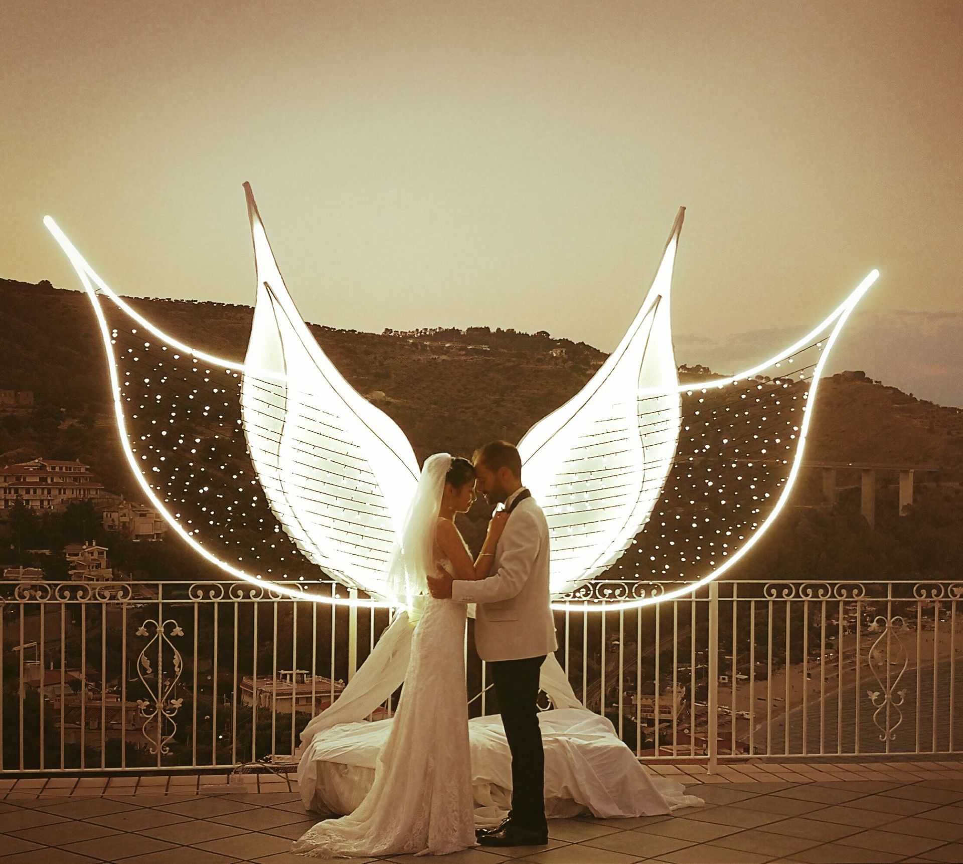 Una sposa e uno sposo posano per una foto con ali fatte di luci