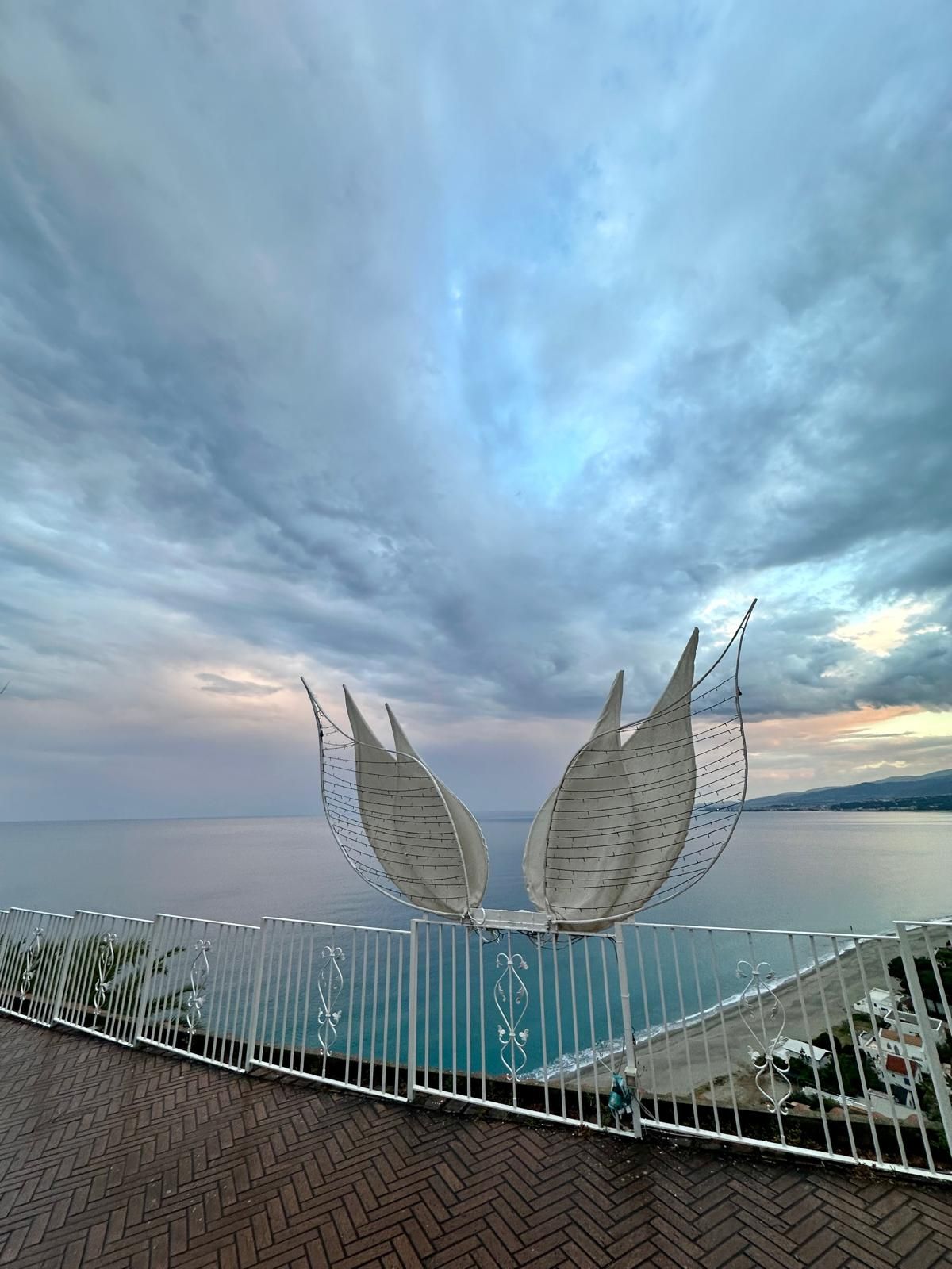 Una statua con le ali è seduta su un balcone che si affaccia sull'oceano.