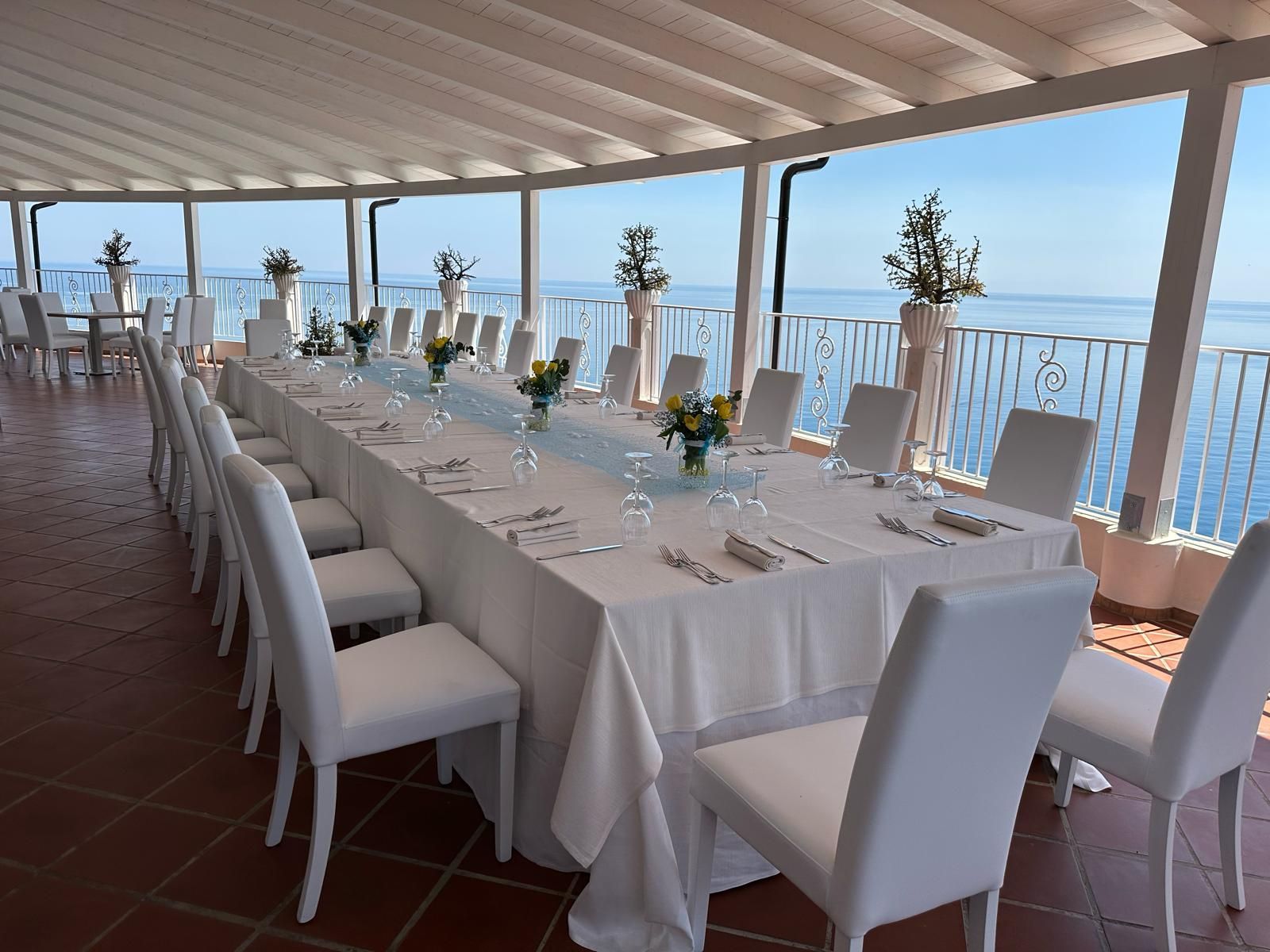 Un lungo tavolo con sedie bianche e vista sull'oceano
