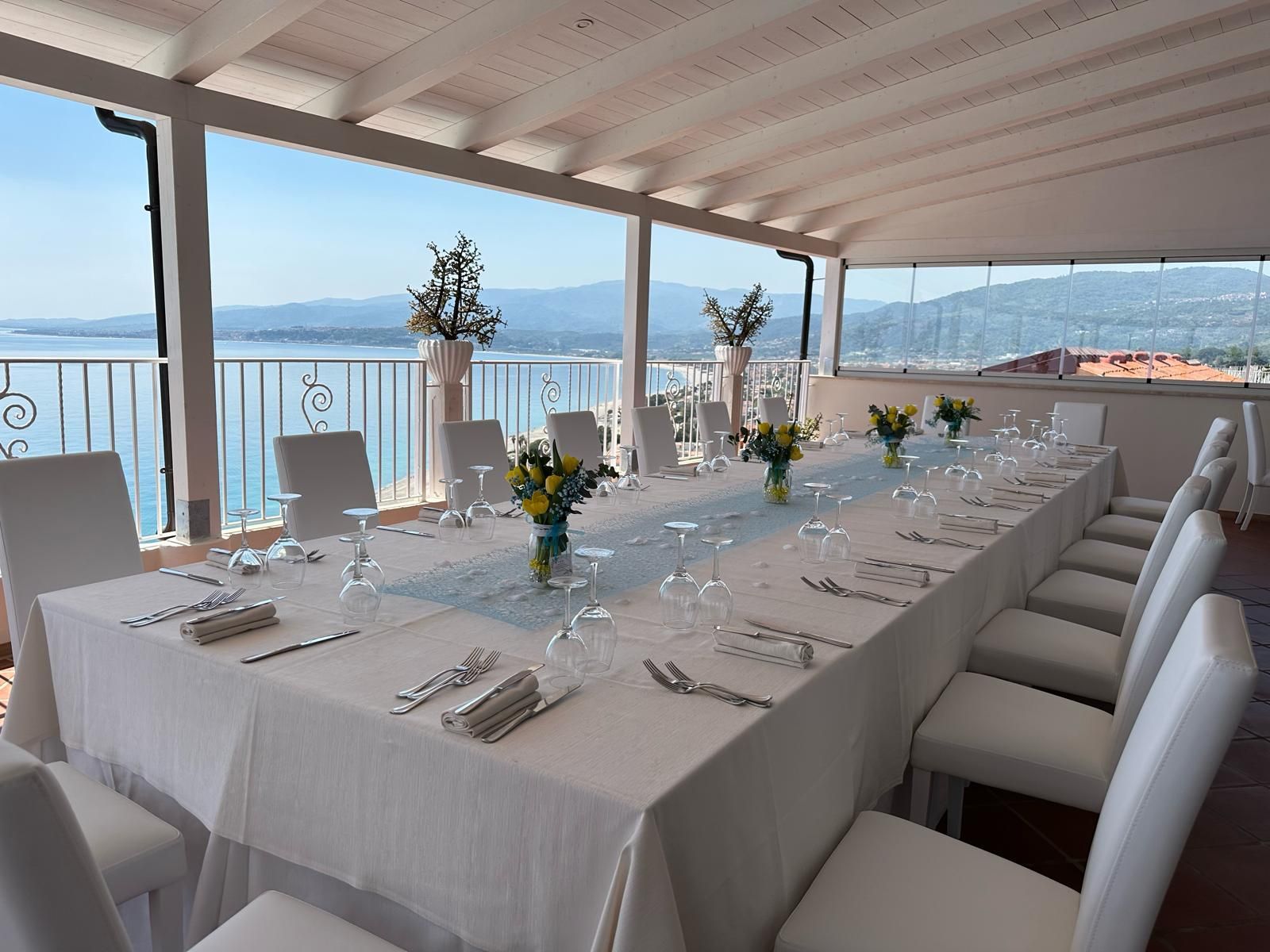 Un lungo tavolo con bicchieri e fiori in una stanza con vista sull'oceano.