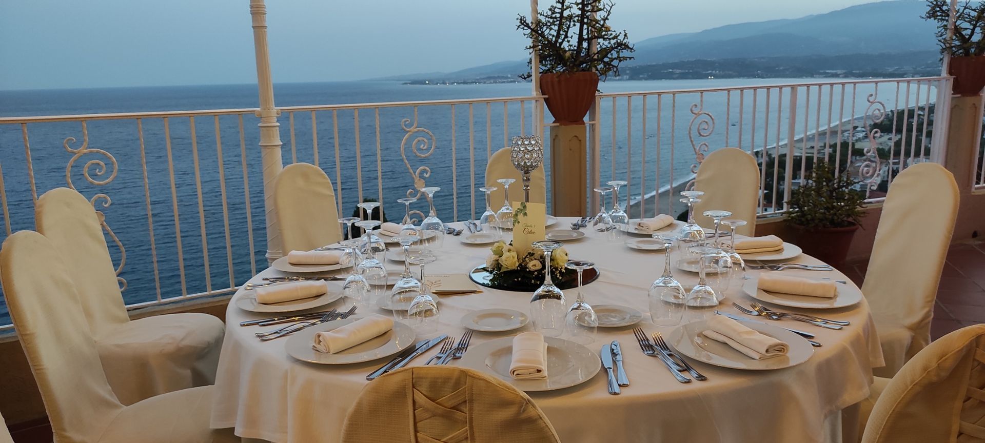 Un tavolo con piatti e bicchieri è posizionato su un balcone che si affaccia sull'oceano.