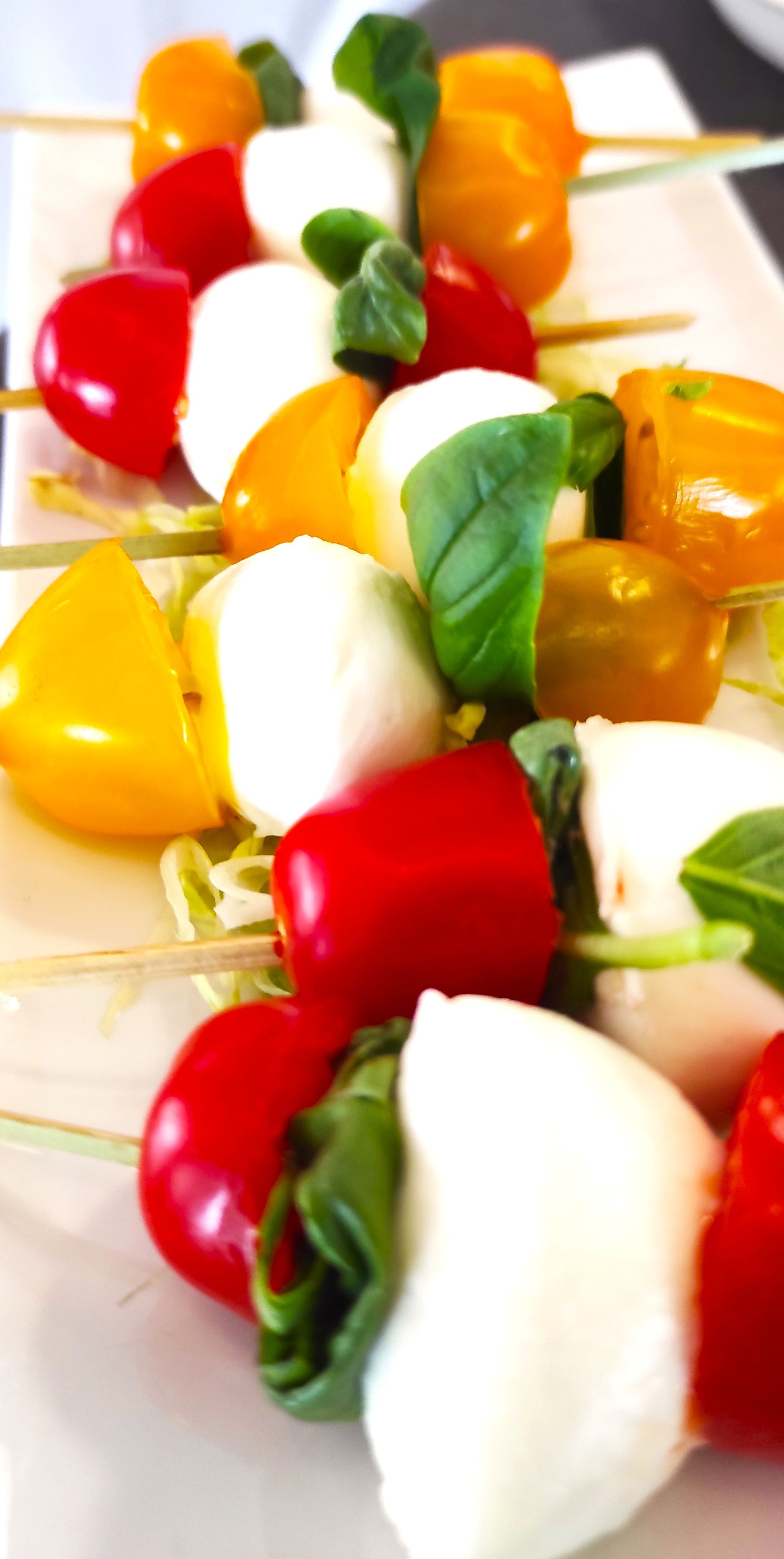 Un piatto bianco condito con pomodori e mozzarella infilzati su spiedini